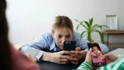 A imagem mostra uma jovem entretida com o smartphone, refletindo sobre O Impacto do Consumo Excessivo de Redes Sociais no Dia a Dia.