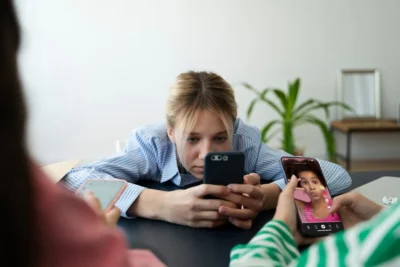 A imagem mostra uma jovem entretida com o smartphone, refletindo sobre O Impacto do Consumo Excessivo de Redes Sociais no Dia a Dia.