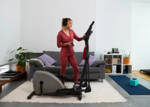 Mulher usando uma bicicleta ergométrica dobrável em casa, com o controle na mão, ideal para quem avalia entre bicicleta ergométrica dobrável e esteira residencial para treinar em casa.