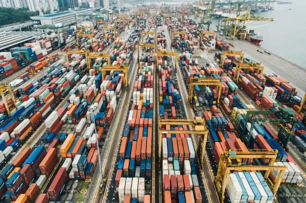 Imagem aérea de um grande porto de cargas com containers coloridos, guindastes e caminhões, ilustrando os desafios e soluções na cadeia de suprimentos industrial.