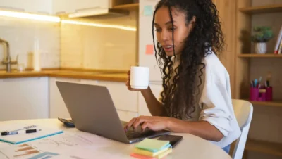 Mulher trabalhando em home office com laptop, rotina de gestão híbrida, produtividade sem microgerenciamento, ambiente organizado.