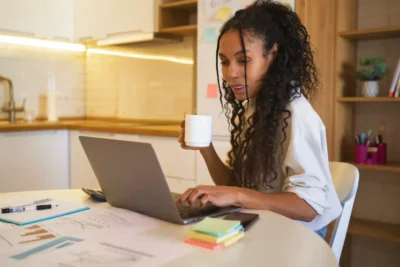 Mulher trabalhando em home office com laptop, rotina de gestão híbrida, produtividade sem microgerenciamento, ambiente organizado.